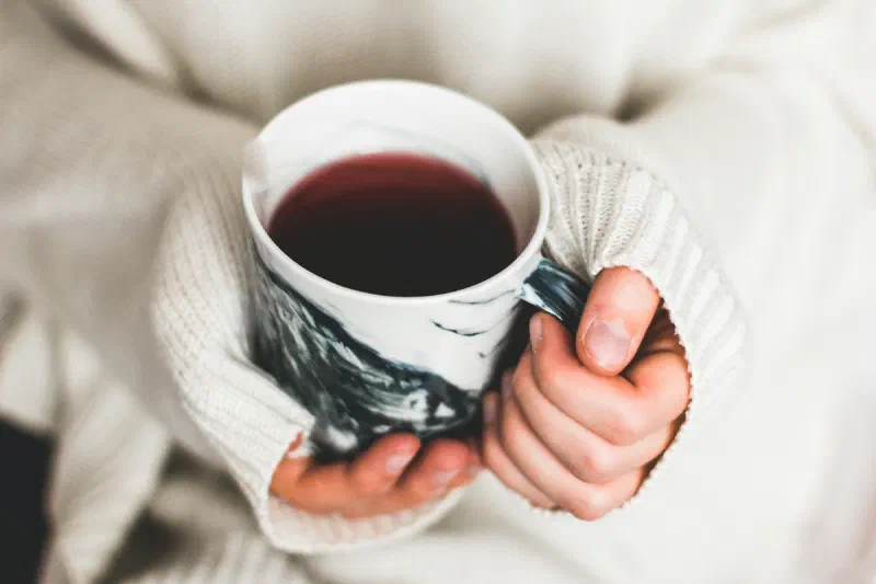 Mãos segurando uma caneca de chá, com um suéter claro