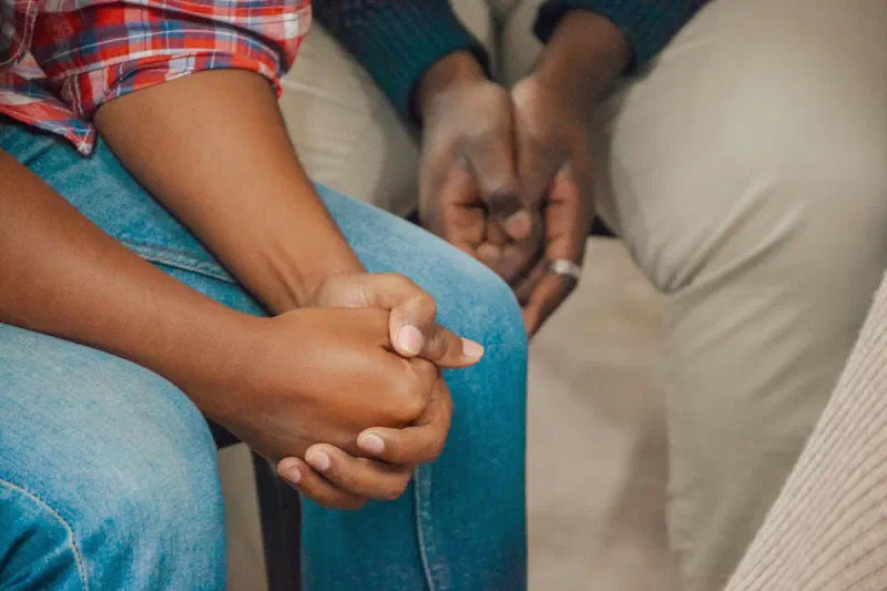 Duas pessoas sentadas lado a lado, de mãos dadas, em um gesto de apoio